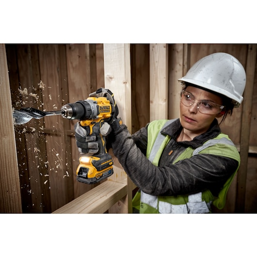 A PERSON USING A DEWALT DCD800 18V XR DRILL DRIVER WITH A COMPACT POWERSTACK BATTERY DRILLING THROUGH TIMBER STUD WALL