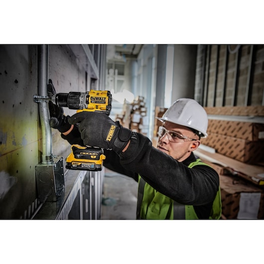 A PERSON USING A DEWALT DCD805 18V XR HAMMER DRILL DRIVER WITH A COMPACT POWERSTACK BATTERY DRILLING A FASTENING HOLE FOR AN ELECTRCAL CLIP