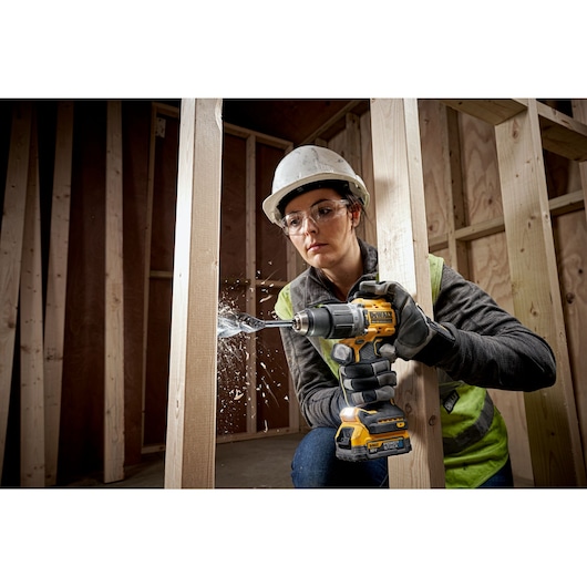 A PERSON USING A DEWALT DCD805 18V XR HAMMER DRILL DRIVER WITH A 2AH BATTERY DRILLING THROUGH TIMBER STUD WALL