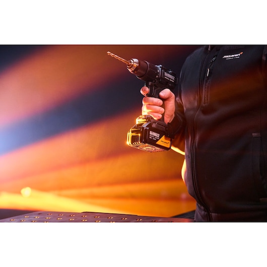 A hand holds the DEWALT x McLaren F1 Team 18V XR Special Edition Hammer Drill Driver with 4Ah battery