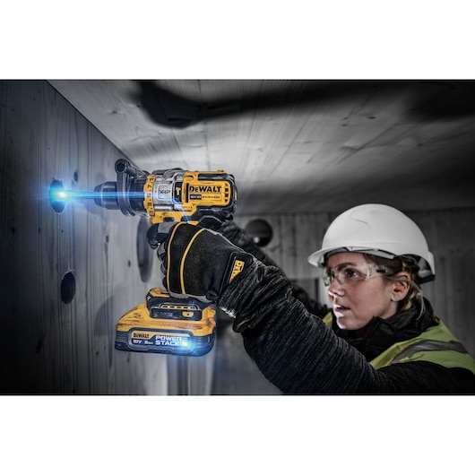 18V XR Brushless drill driver cutting hole into wooden wall. A blue light effect illustrates Powerstack battery power