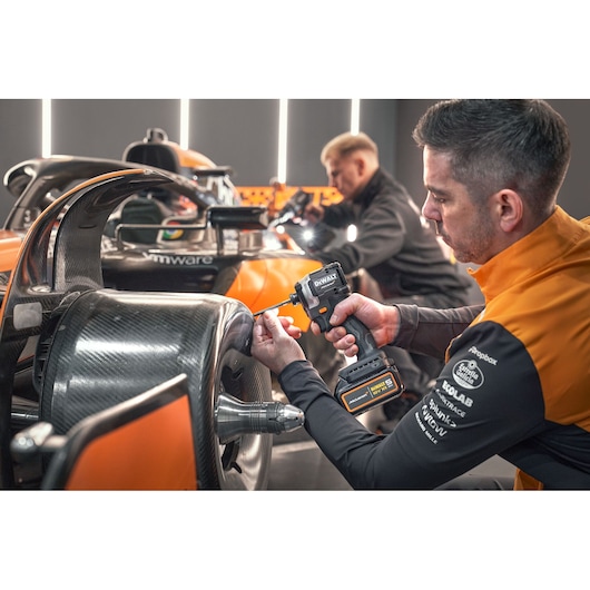 McLaren mechanic using DEWALT/McLaren impact driver on McLaren racing car; another mechanic works in the background