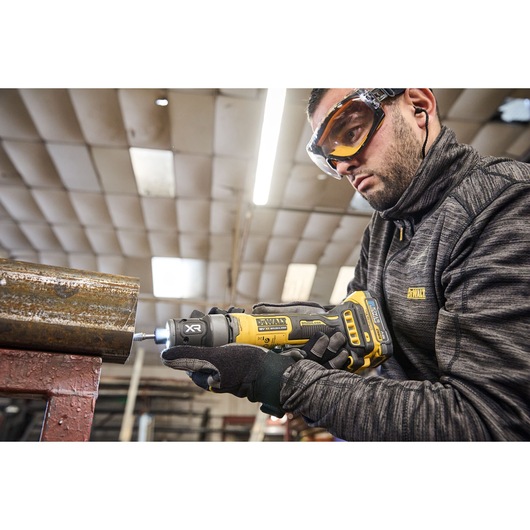 Worker uses the DEWALT 18V XR Compact Inline Grinder to smooth a metal surface