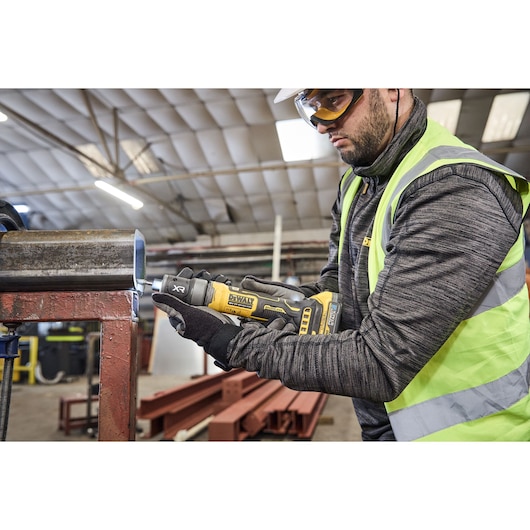 Worker uses the DEWALT 18V XR Compact Inline Grinder to smooth a metal surface