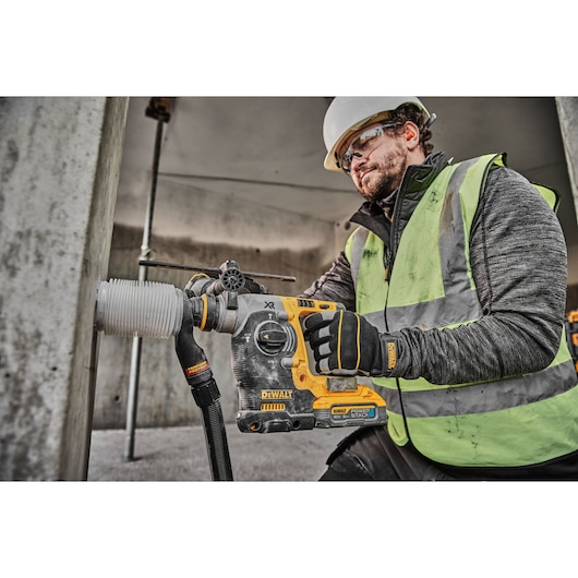 18V XR Brushless SDS-Plus Hammer Drill drilling into concrete wall using a dust extractor