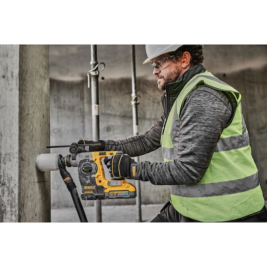 18V XR Brushless SDS-Plus Hammer Drill drilling into concrete wall using a dust extractor