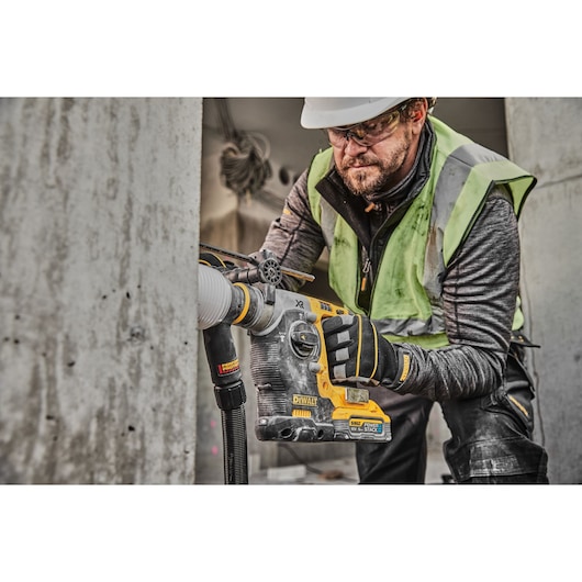 18V XR Brushless SDS-Plus Hammer Drill drilling into concrete wall using a dust extractor