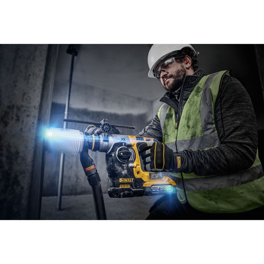 18V XR Brushless SDS-Plus Hammer Drill drilling into concrete wall using a dust extractor.