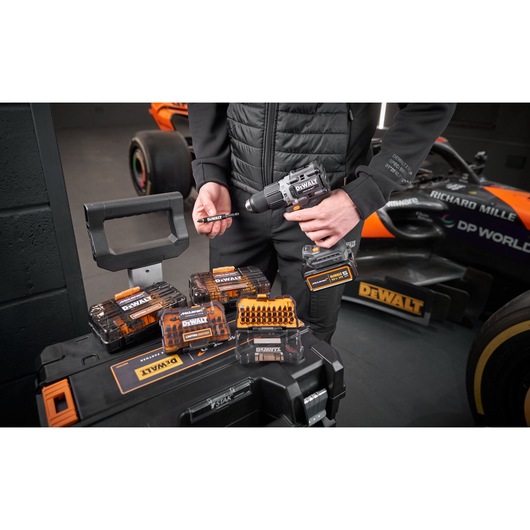 x4 Limited Edition DEWALT/McLaren screwdriver bit sets sit on top of a Tstak box, behing which a McLaren mechanic stands holding a impact driver and bit holder.