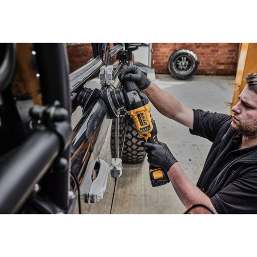 A person wearing black gloves uses a DEWALT cordless polisher to polish the side of a black vehicle in a garage setting.