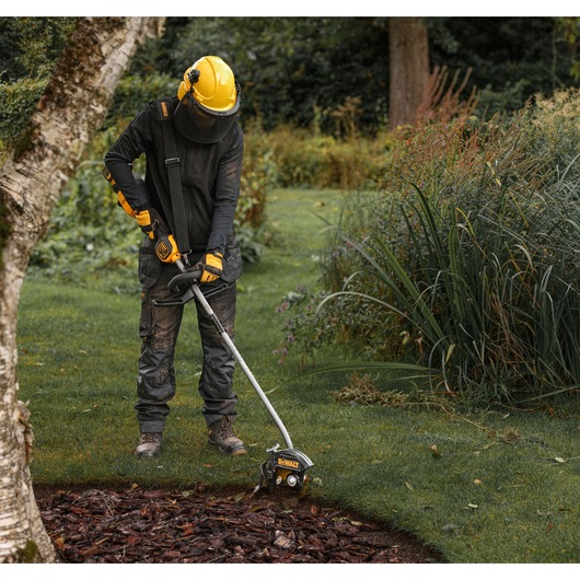 Worker using  a DEWALT split boom with the DEWALT DCMASED9N Edger Attachment to trim grass edging