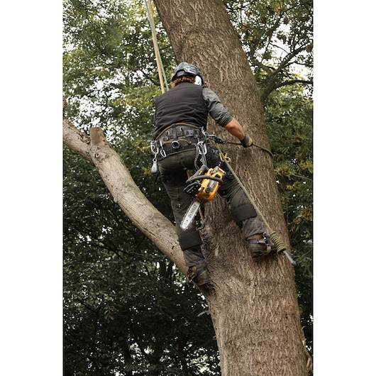 Arborist climbing a tree with the DEWALT 54V XR FLEXVOLT Compact Top Handle Chainsaw attached for use