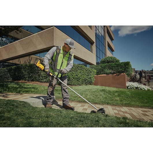 Worker using the DEWALT 54V XR FLEXVOLT Straight Shaft Edger to trim lawn edge