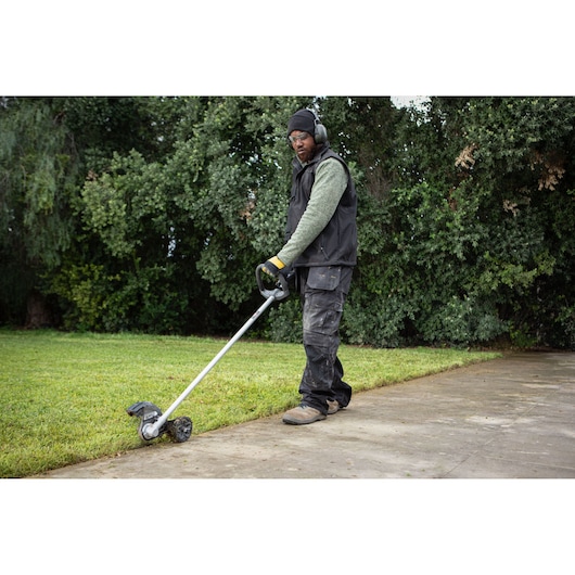 Worker using a DEWALT 54V XR FLEXVOLT Straight Shaft Edger to trim the edge of a lawn 