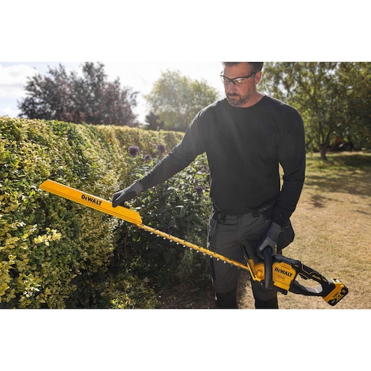 Worker attaching the DEWALT hedge sweep attachment to the DEWALT 18V XR Brushless Hedge Trimmer