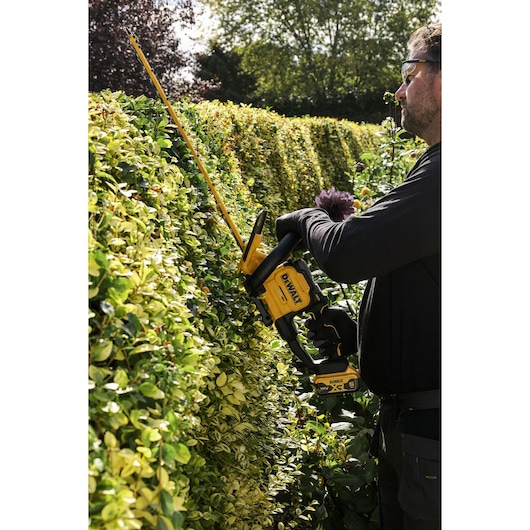 Worker trimming a hedge using  the DEWALT 18V XR Brushless Hedge Trimmer 