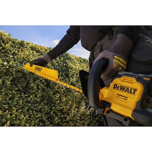 Worker attaching the DEWALT hedge sweep attachment to the DEWALT 18V XR Brushless Hedge Trimmer