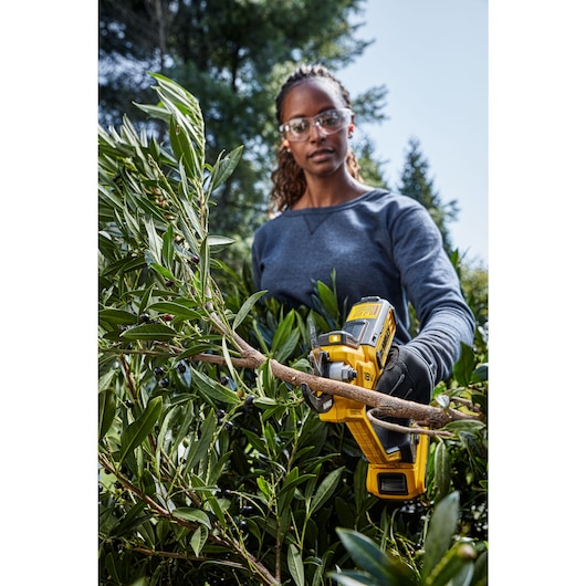 Female user trimming heavy brush using powered cordless pruner