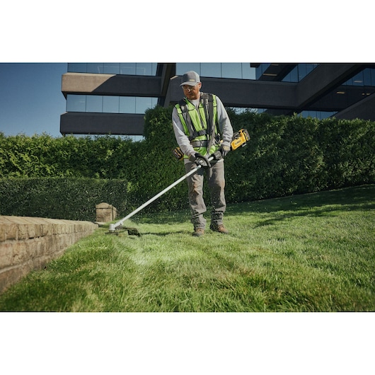 Worker using the DEWALT 54V XR FLEXVOLT String Trimmer Lite to cut grass