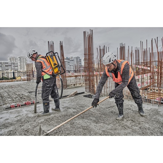 Workers pouring and raking on concrete. Concrete is being poured using Powershift Backpack Concrete Vibrator