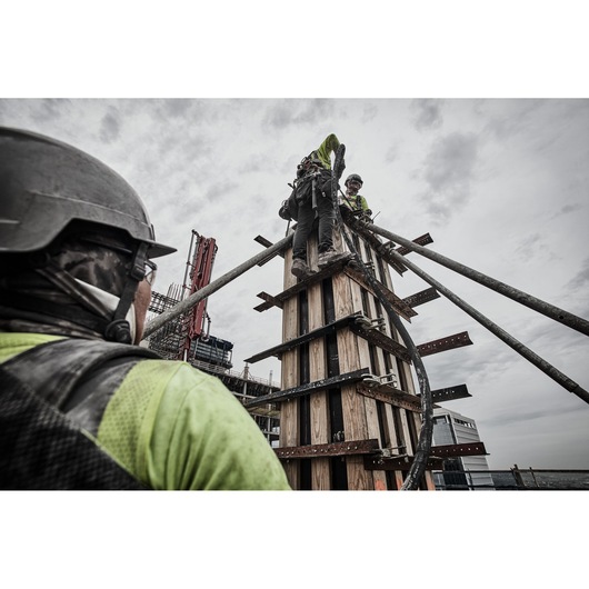 Construction workers with hose at the top of a tall wooden concrete frame. A third construction worker is close to camera.