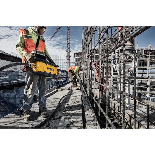 Two construction workers use Powershift Powerpack Concrete Vibrator and hose to pour concerte into a channel