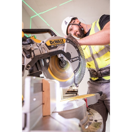 The DEWALT 18V XR 305mm Slide Mitre Saw being used on job site by worker in high visibility vest, safety goggles and helmet, worker is cutting through wooden beam.