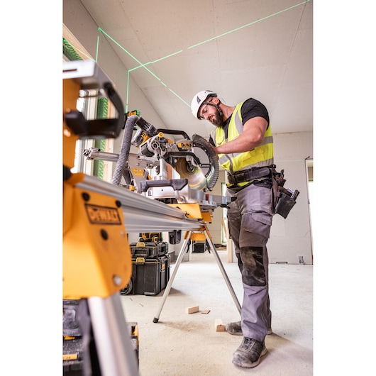 The DEWALT 18V XR 305mm Slide Mitre Saw being used on job site by worker in high visibility vest, safety goggles and helmet, worker is cutting through wooden beam.
