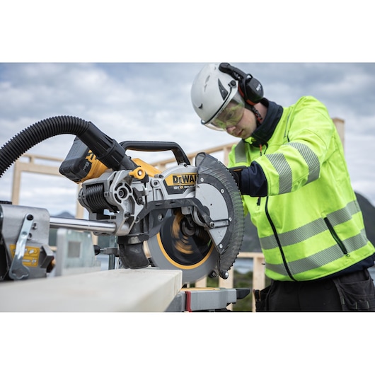 The DEWALT 18V XR 305mm Slide Mitre Saw being used by worker with safety goggles, hat and ear defenders to cut through timber beam outdoors