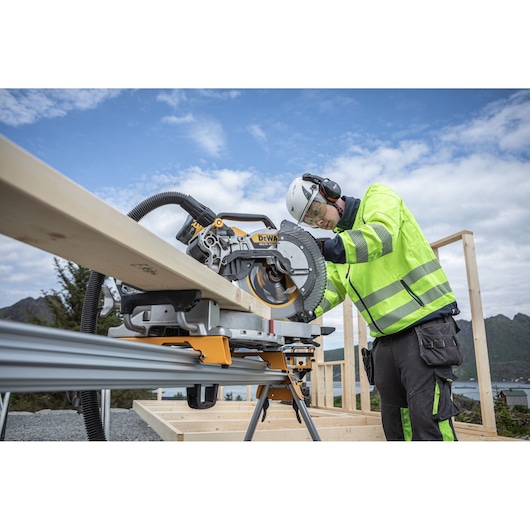 The DEWALT 18V XR 305mm Slide Mitre Saw being used by worker with safety goggles, hat and ear defenders to cut through timber beam outdoors