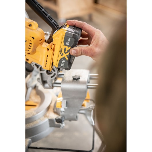 Carpenter adding 8Ah battery to the DEWALT 18V XR 305mm Slide Mitre Saw in wood shop
