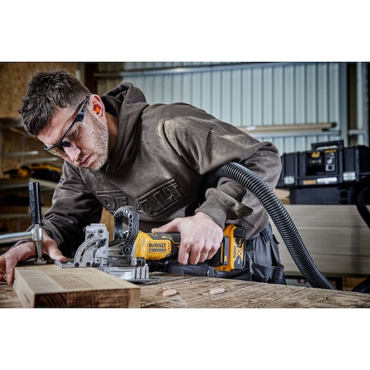 A PERSON USING A DCW682 18V XR BISCUIT JOINTER WITH A 5AH BATTERY ON OAK TIMBER IN A WORKSHOP