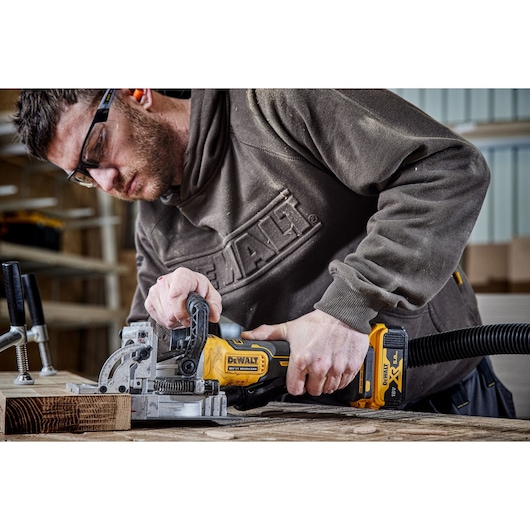 A PERSON USING A DCW682 18V XR BISCUIT JOINTER WITH A 5AH BATTERY ON OAK TIMBER IN A WORKSHOP