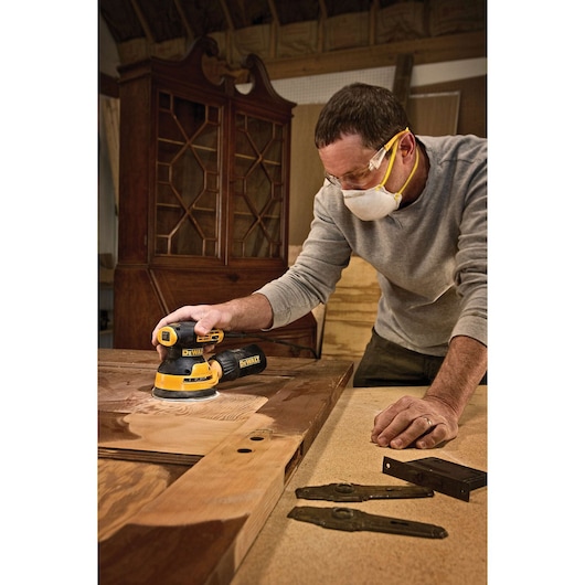 5 inch variable speed random orbit sander in action in use to sand a wooden sheet by a worker.