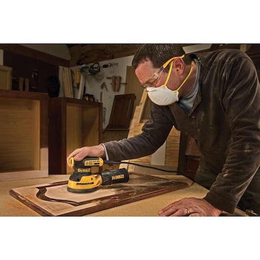 5 inch variable speed random orbit sander being used to sand a small wooden panel by a worker.
