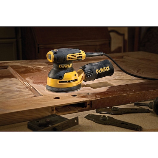 5 inch variable speed random orbit sander placed on top of a wooden sheet at a worksite.