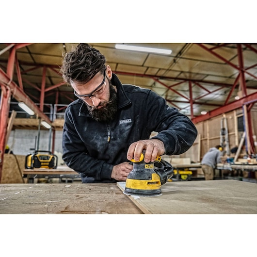 5 inch variable speed random orbit sander placed on top of a wooden sheet at a worksite.