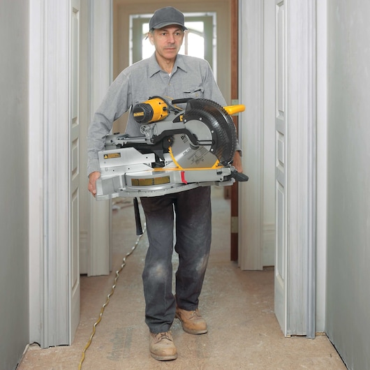12 inch double bevel sliding compound miter saw being carried by a worker at a worksite.