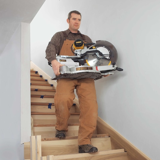12 inch double bevel sliding compound miter saw being carried down stairs by a worker.