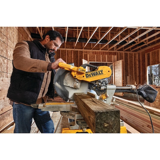 12 inch double bevel sliding compound miter saw being used to cut a thick piece of wood by a worker.