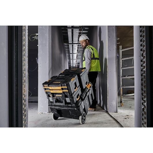 Construction worker pulling a mobile TSTAK job chest along a corridor on a construction site. The chest has x3 Tstak cases connected on top of it