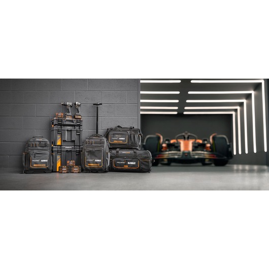 Limited Edition DEWALT/McLaren storage bags, Tstak trolley, impacts and accessory boxes stand in front of a grey wall. A McLaren racing car is on the right in the background.