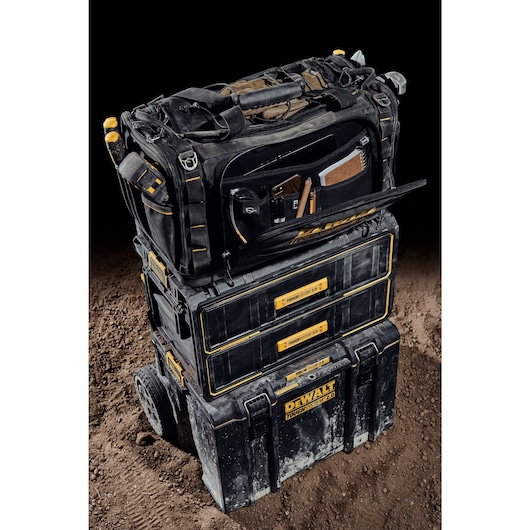 Front view of the DEWALT TOUGHSYSTEM 2.0 22-inch jobsite soft storage toolbag with front pocket open holding various tools on top of TOUGHSYSTEM 2.0 two-drawer organizer.