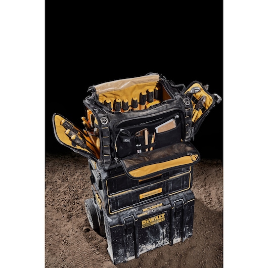 Three quarter view of the DEWALT TOUGHSYSTEM 2.0 22-inch jobsite soft storage toolbag with open front pocket holding notebook, phone and pencils sitting on TOUGHSYSTEM 2.0 two-drawer organizer.
