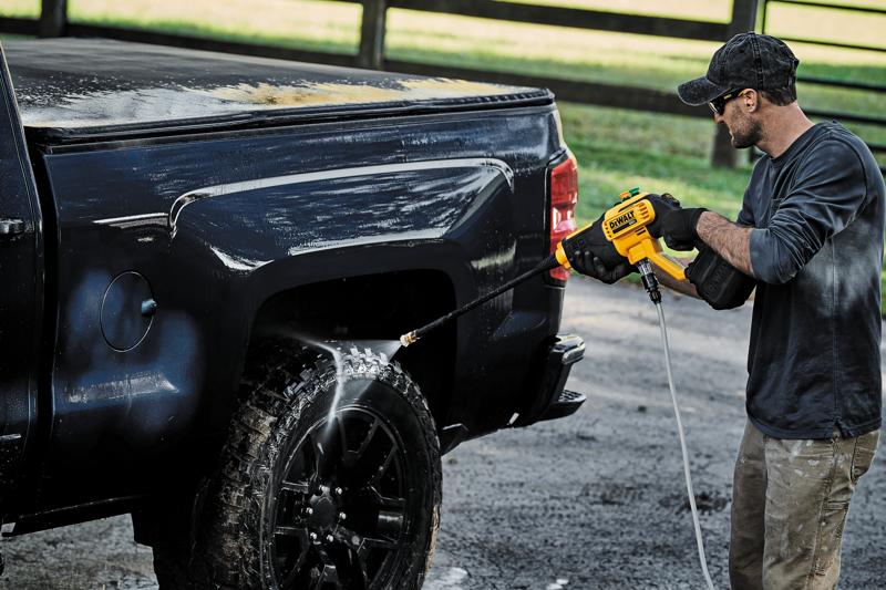 En person använder en DEWALT DCPW550B batteridriven högtryckstvätt för att rengöra hjulet och sidan på en svart pickup utomhus.